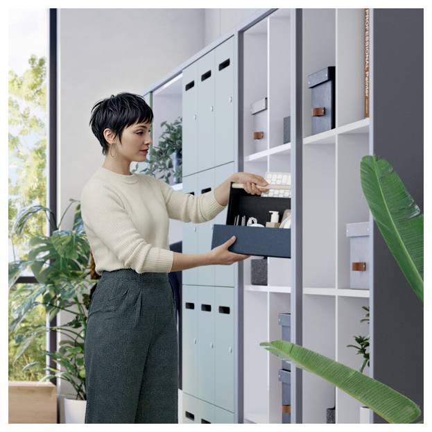 Femme organisant des fournitures de bureau dans une armoire de rangement, tirant une boîte d'une étagère ouverte dans un bureau lumineux.