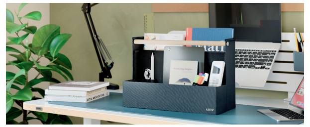 Espace de travail de bureau avec un organiseur noir contenant des livres, des post-it et des fournitures de bureau devant un ordinateur portable et une plante.
