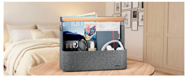 Organisateur de bureau en feutre gris sur une table avec des livres, une montre, des écouteurs et des stylos ; fond de chambre à coucher avec lit et photos murales.