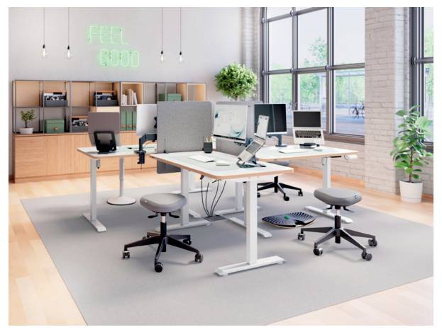 Bureau moderne en plan ouvert avec des bureaux ajustables, des ordinateurs, des tabourets et une enseigne au néon « FEEL GOOD » sur le mur du fond.