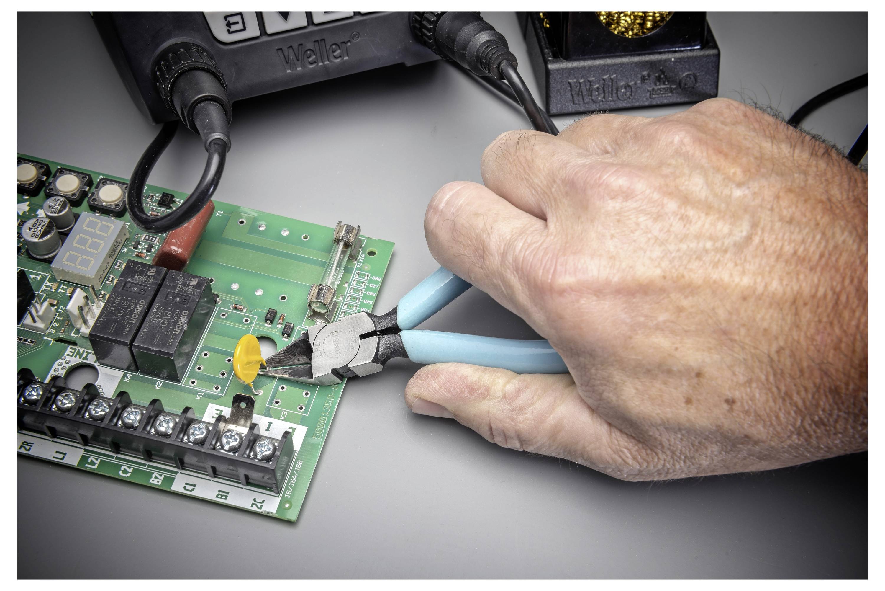 Main utilisant une pince pour ajuster ou couper un fil sur une carte de circuit électronique lors d'un travail de réparation.