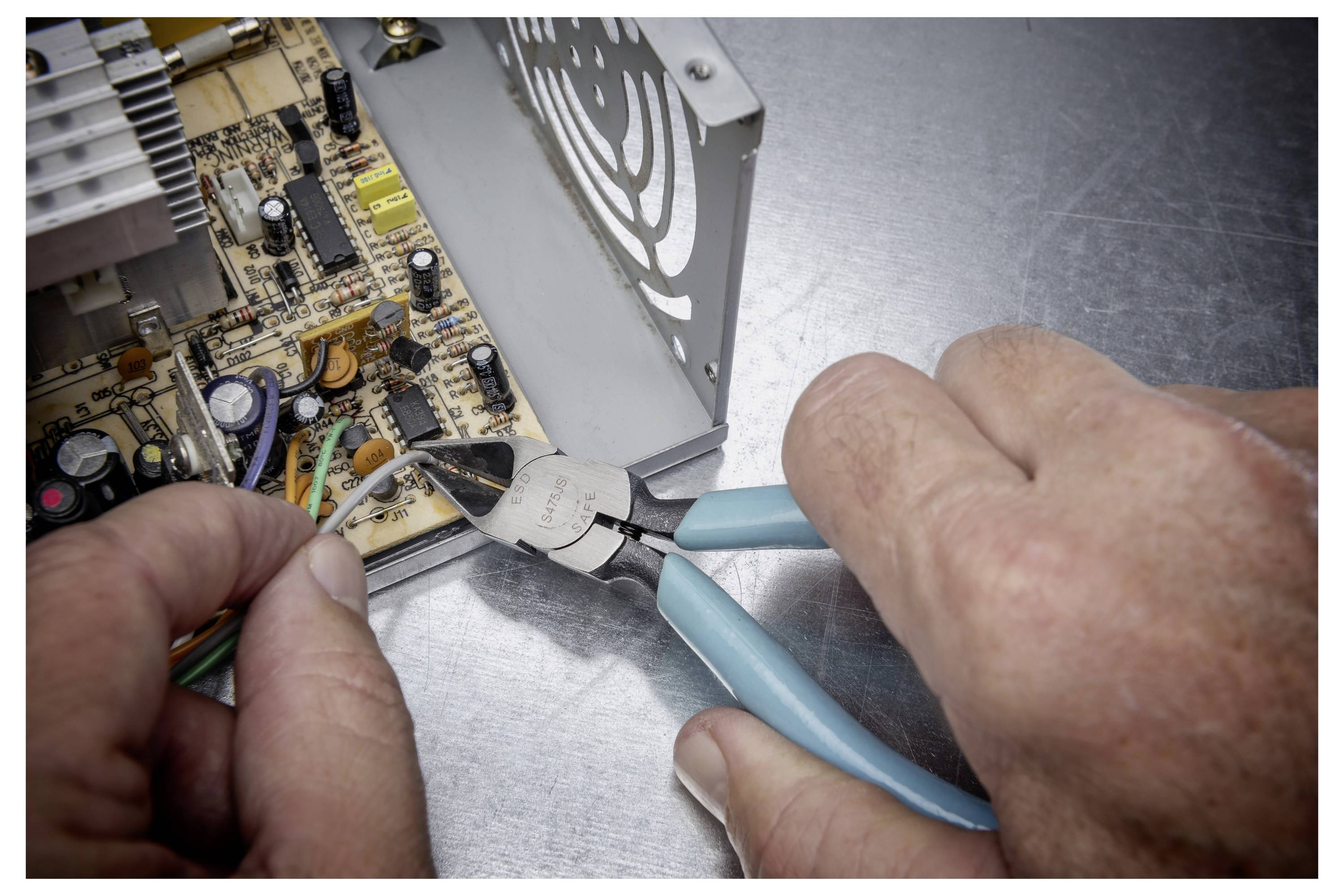 Mains utilisant des pinces pour couper des fils lors de la réparation d'une carte de circuit à l'intérieur d'un appareil électronique.