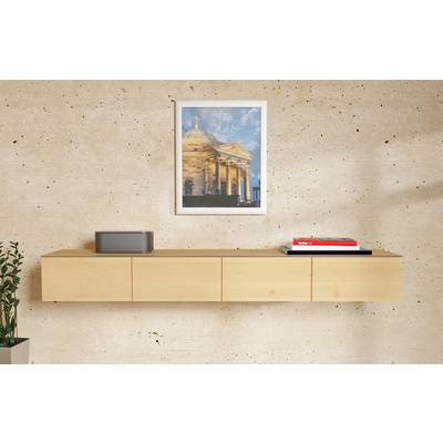 Pièce minimaliste avec un meuble suspendu en bois, une photo de bâtiment encadrée au-dessus, un petit haut-parleur sur la gauche et des livres empilés sur la droite contre un mur texturé.