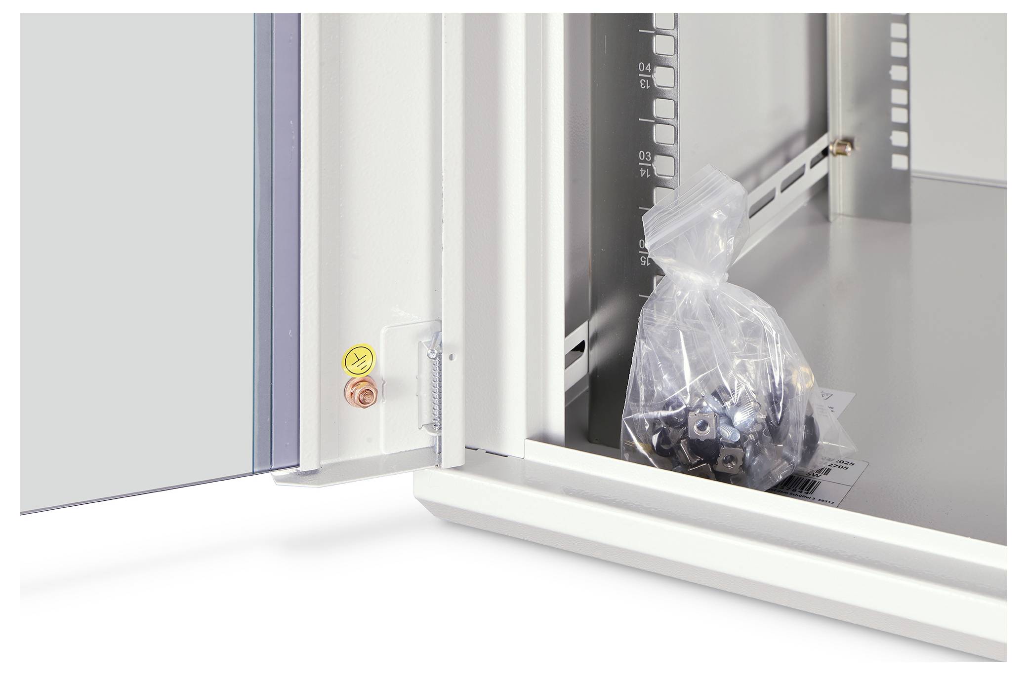 Un sac en plastique transparent contenant de petites pièces métalliques repose à l'intérieur d'une armoire industrielle ouverte ou d'une enceinte de machine.