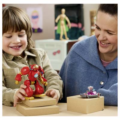 Un enfant souriant et un adulte jouent avec de petits jouets robots sur des boîtes à une table dans une salle de classe ou une salle de jeux.