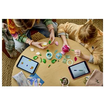 Les enfants sont assis autour d'une table en train d'assembler des pièces d'artisanat colorées et des perles tout en utilisant deux tablettes, ce qui suggère une activité créative collaborative ou un jeu.
