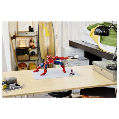 Figurine d'action Spider-Man posée sur un bureau dans une chambre à coucher, avec une petite figurine à côté et une planche à roulettes et une lampe en arrière-plan.