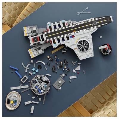 Vue de dessus d'un modèle de vaisseau spatial LEGO en cours d'assemblage, avec des pièces dispersées et des figurines LEGO sur une table bleue.