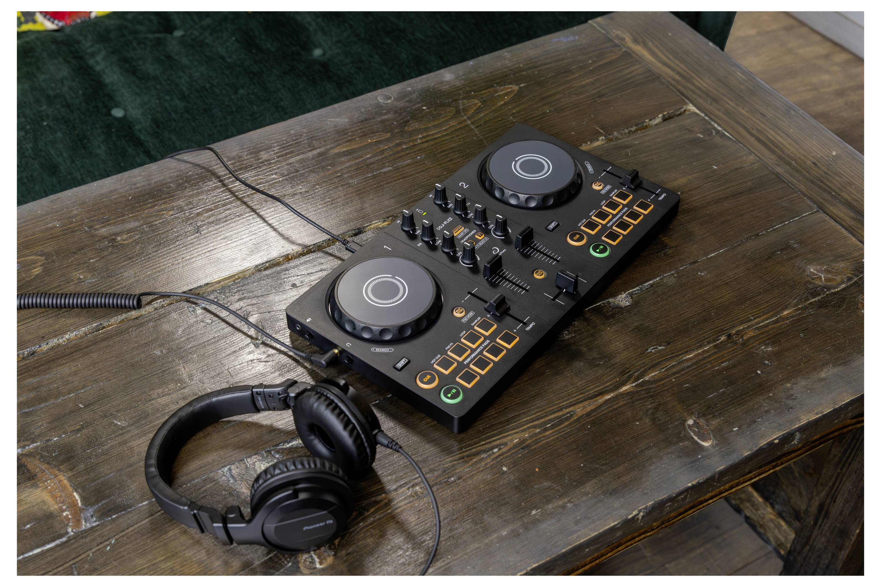Contrôleur DJ avec deux platines de mixage, des boutons éclairés et un casque audio attaché reposant sur une table en bois.