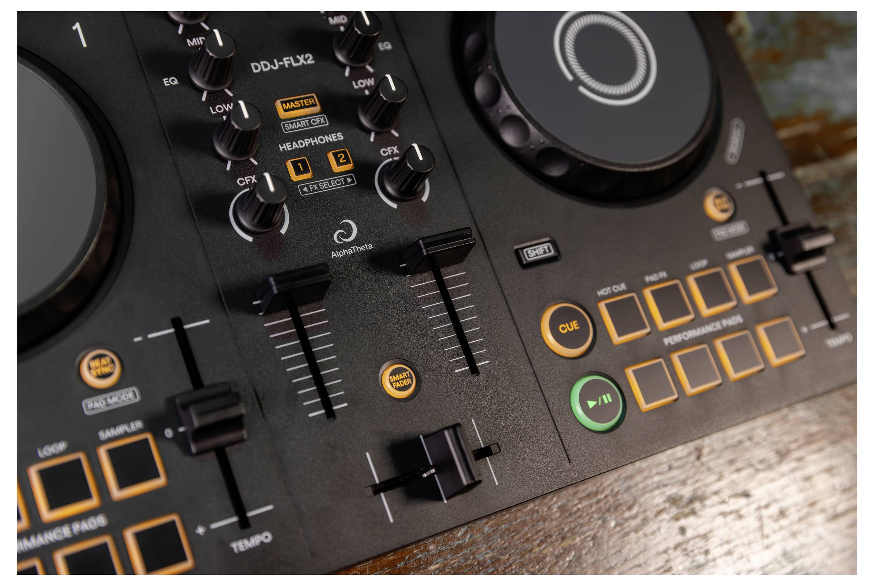 Gros plan d'une console DJ avec une molette de contrôle, des curseurs, des boutons de réglage et des boutons de repère/lecture illuminés sur une surface en bois.