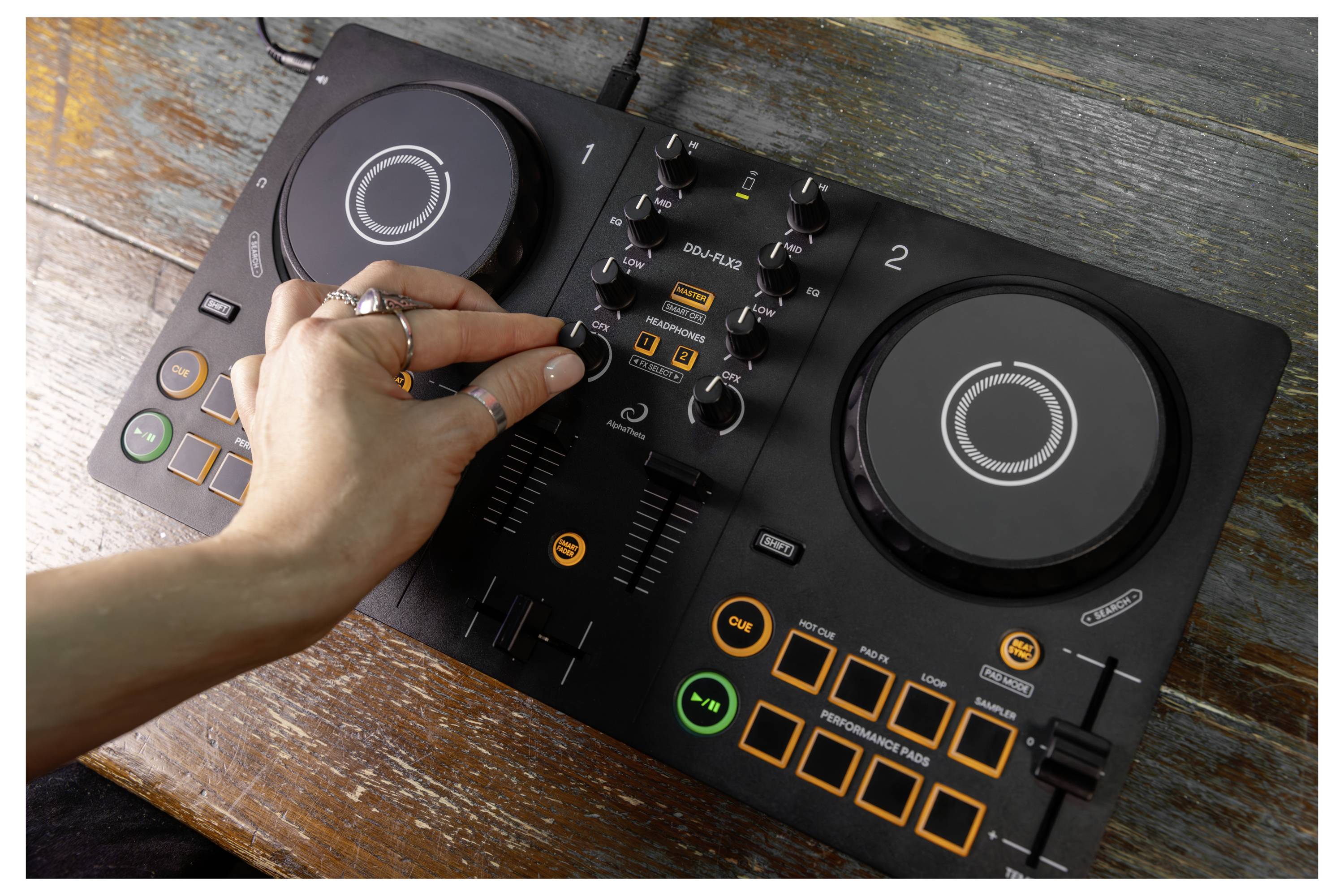 Ajustement manuel des contrôles sur une table de mixage DJ Rane noire avec deux molettes de navigation et des boutons illuminés sur une table en bois.
