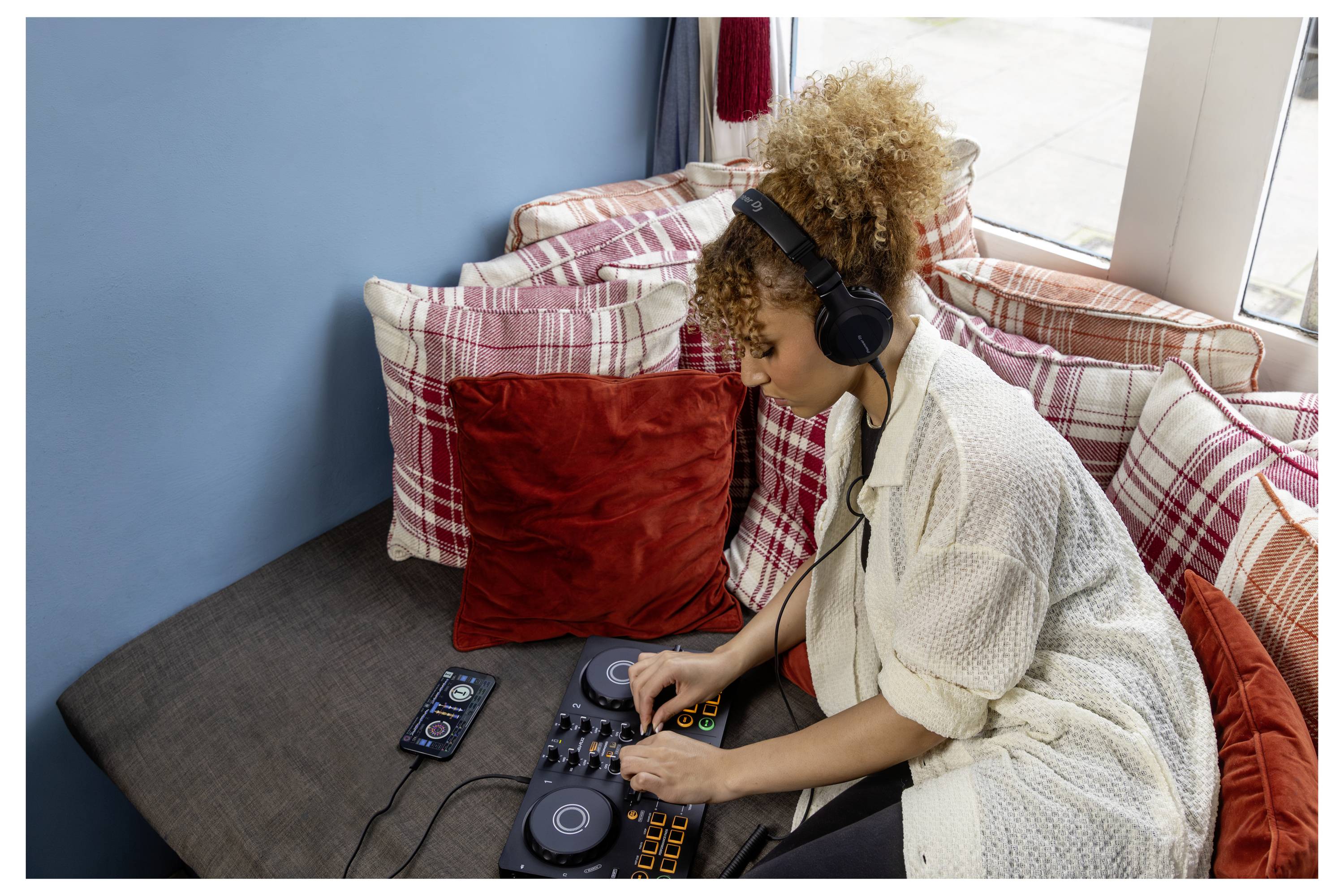 Jeune femme portant des écouteurs mixe la musique sur une table de mixage DJ à côté d'un canapé dans un salon.