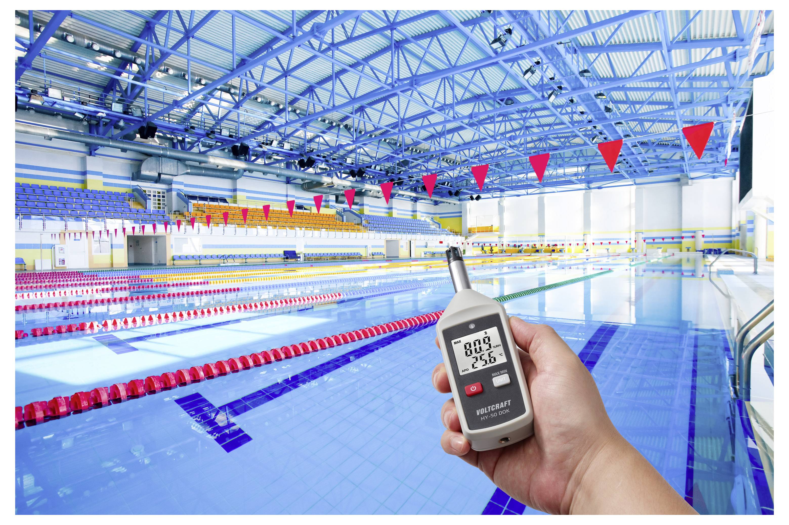 Main tenant une sonomètre numérique affichant 68,9 dB et 25,8°C à l'intérieur d'une piscine intérieure avec des couloirs et des fanions rouges.