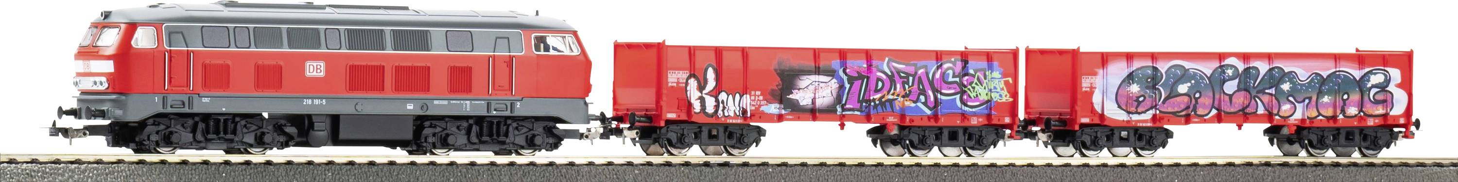 Une locomotive rouge et grise se déplace le long d'une voie ferrée, couverte de graffitis colorés sur le côté.