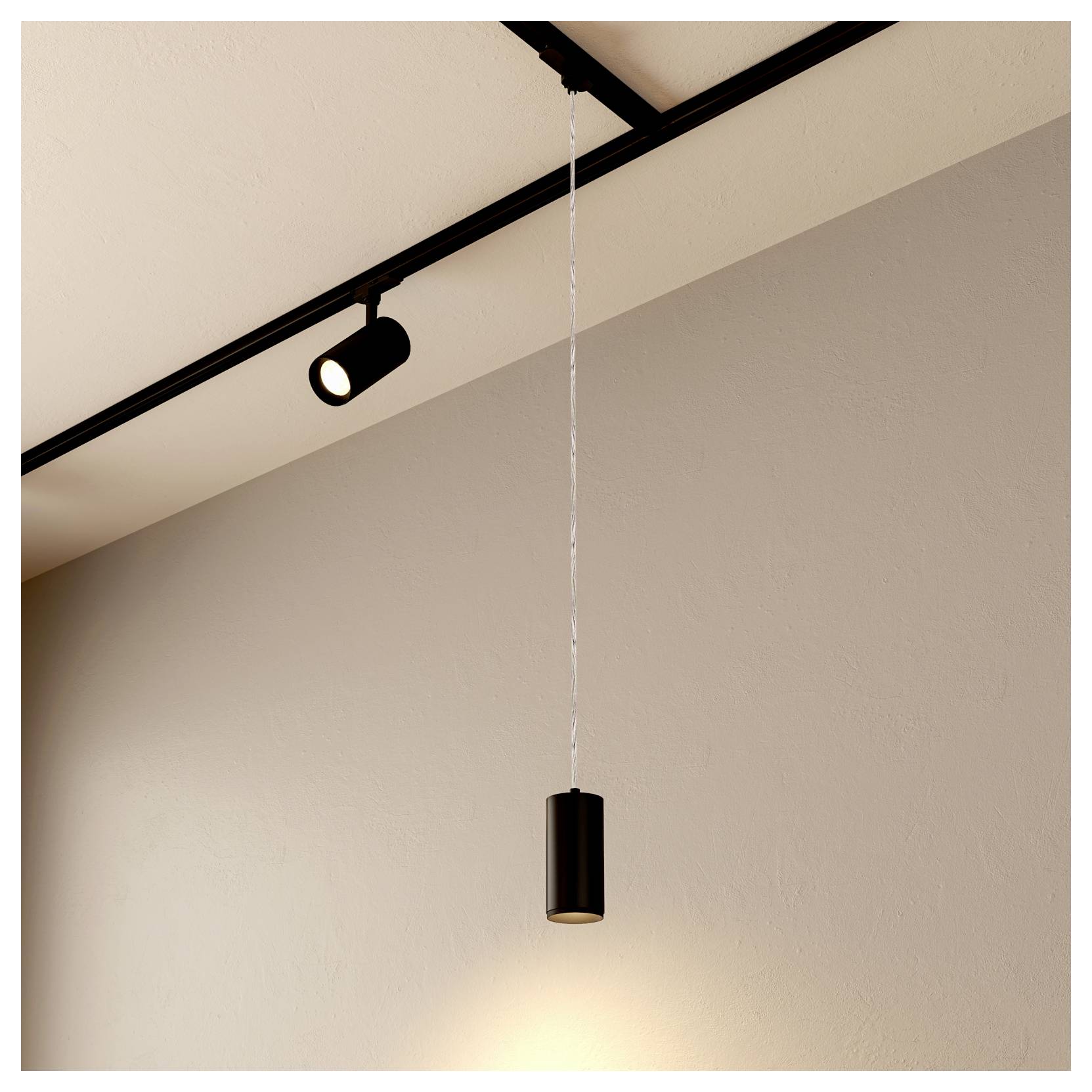 Un suspension cylindrique noire pend d'un rail de plafond, éclairant un mur beige uni.