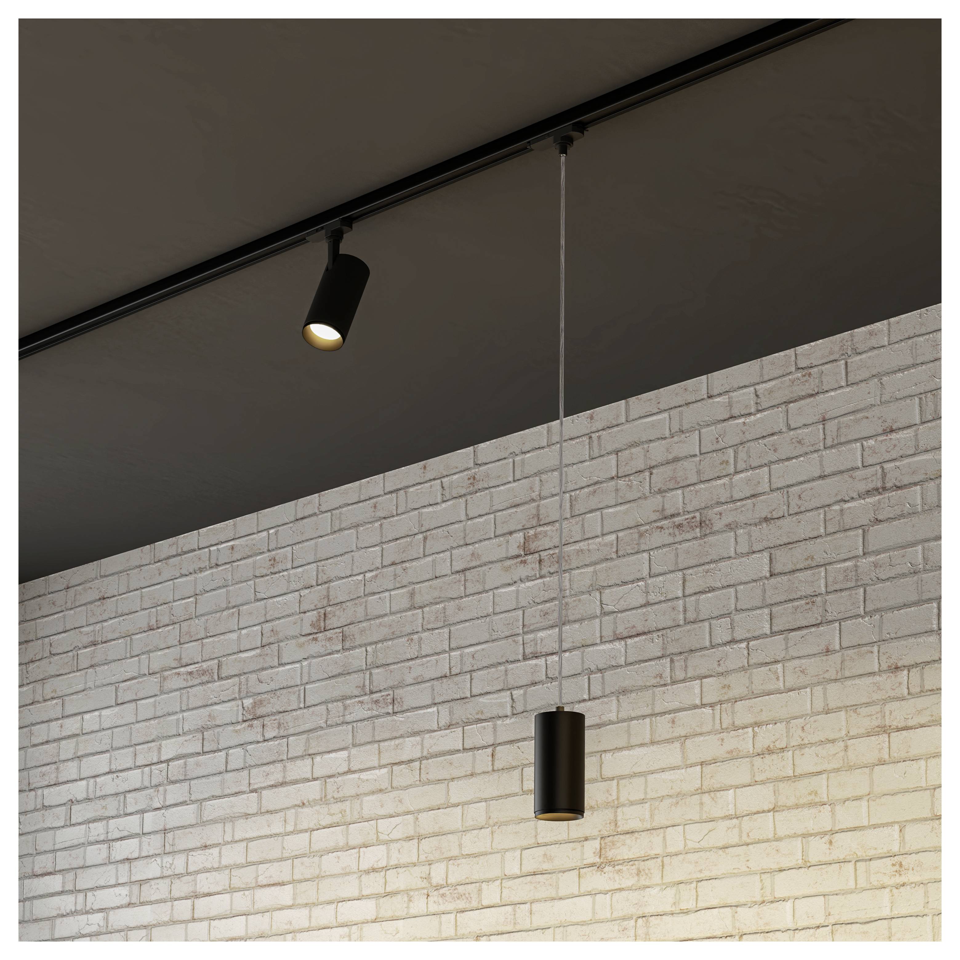 Luminaires de type rail et suspensions sur un plafond incliné au-dessus d'un mur gris, avec un projecteur qui s'illumine.
