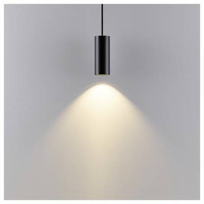 Luminaire suspendu cylindrique noir projetant un cône de lumière chaleureuse sur un mur gris uni.