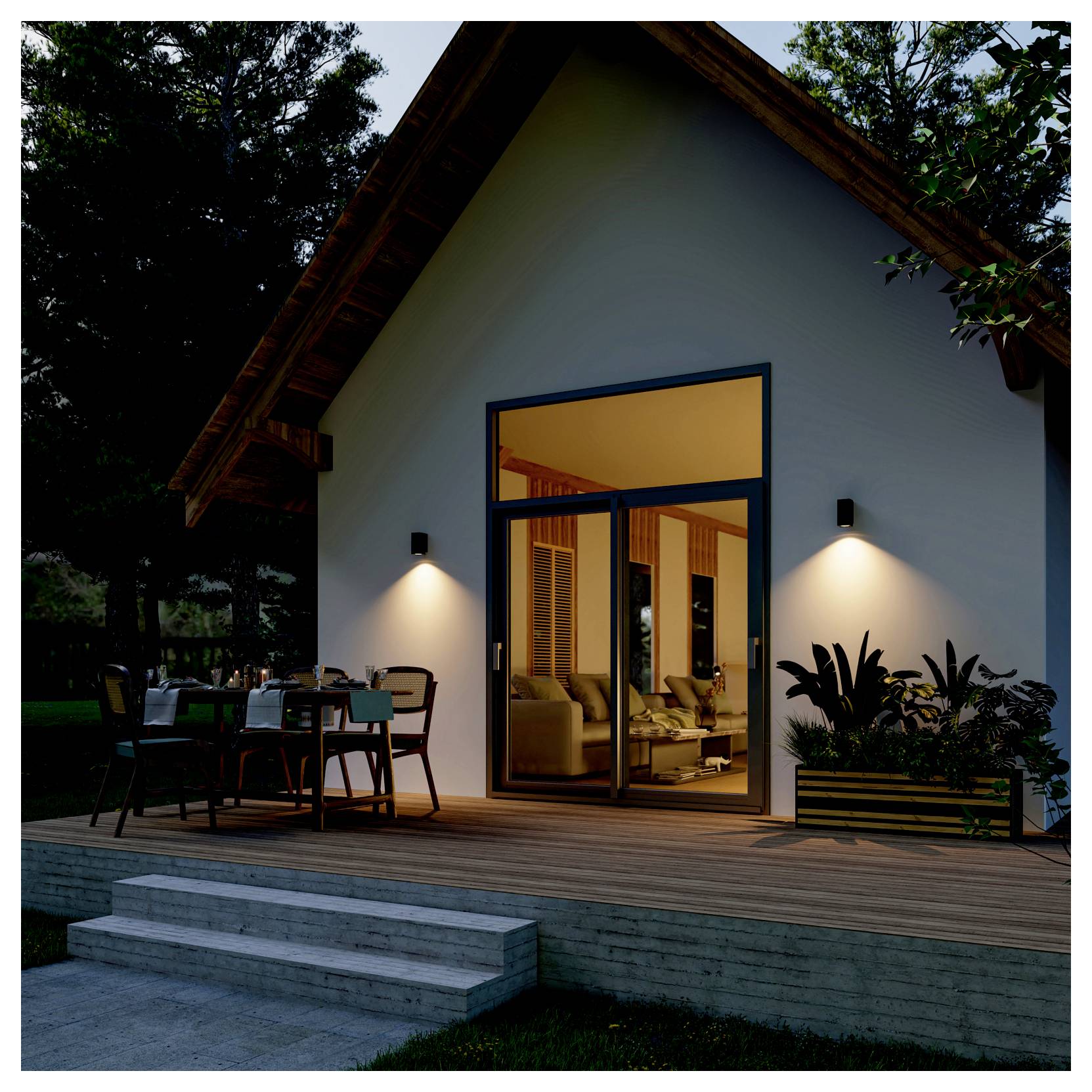 Maison moderne en A au crépuscule, avec terrasse éclairée, portes-fenêtres ouvertes, salon de jardin et intérieur chaleureux visible depuis la terrasse.