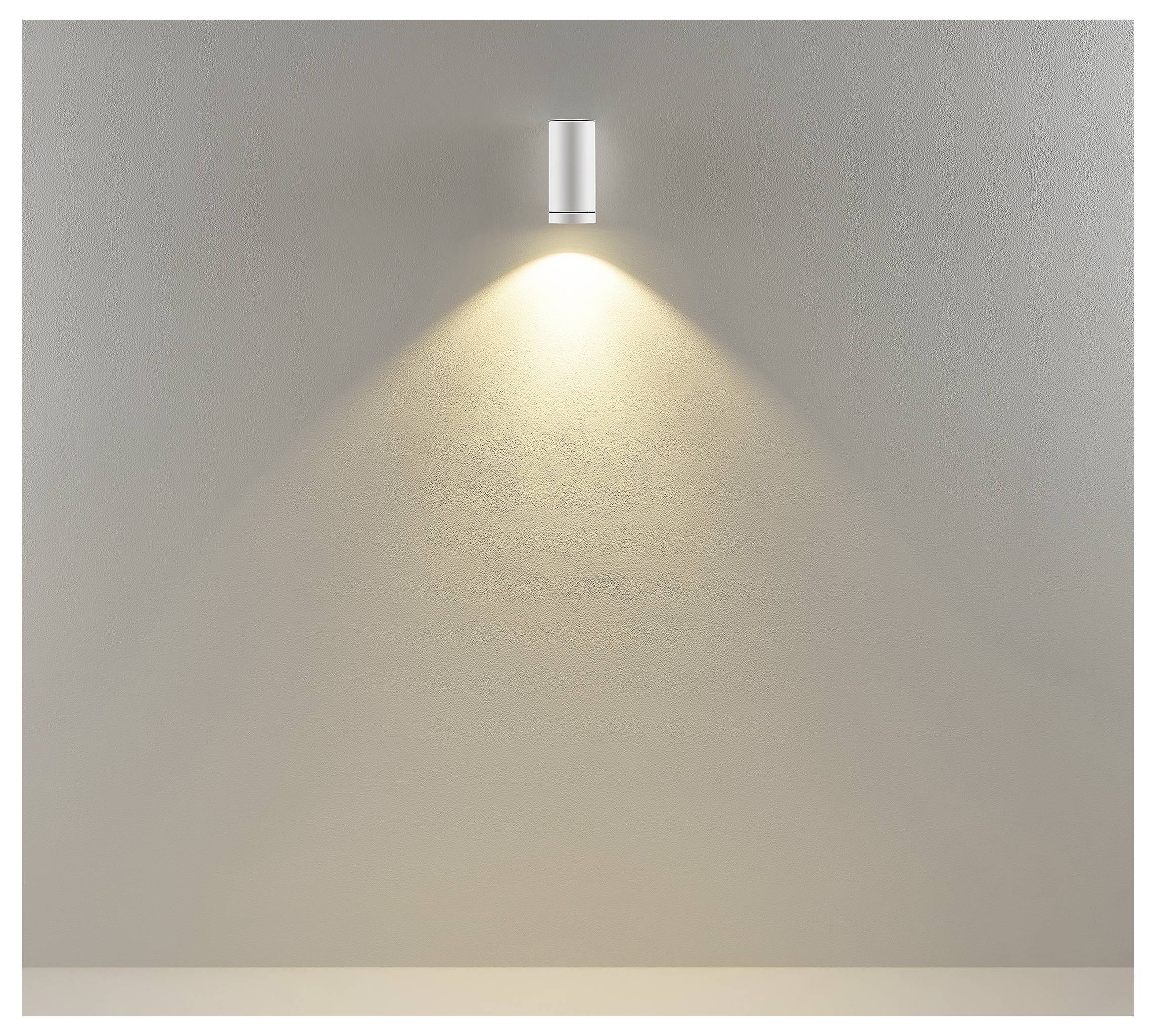 Luminaire cylindrique mural projetant un faisceau chaud vers le bas sur un mur beige uni.