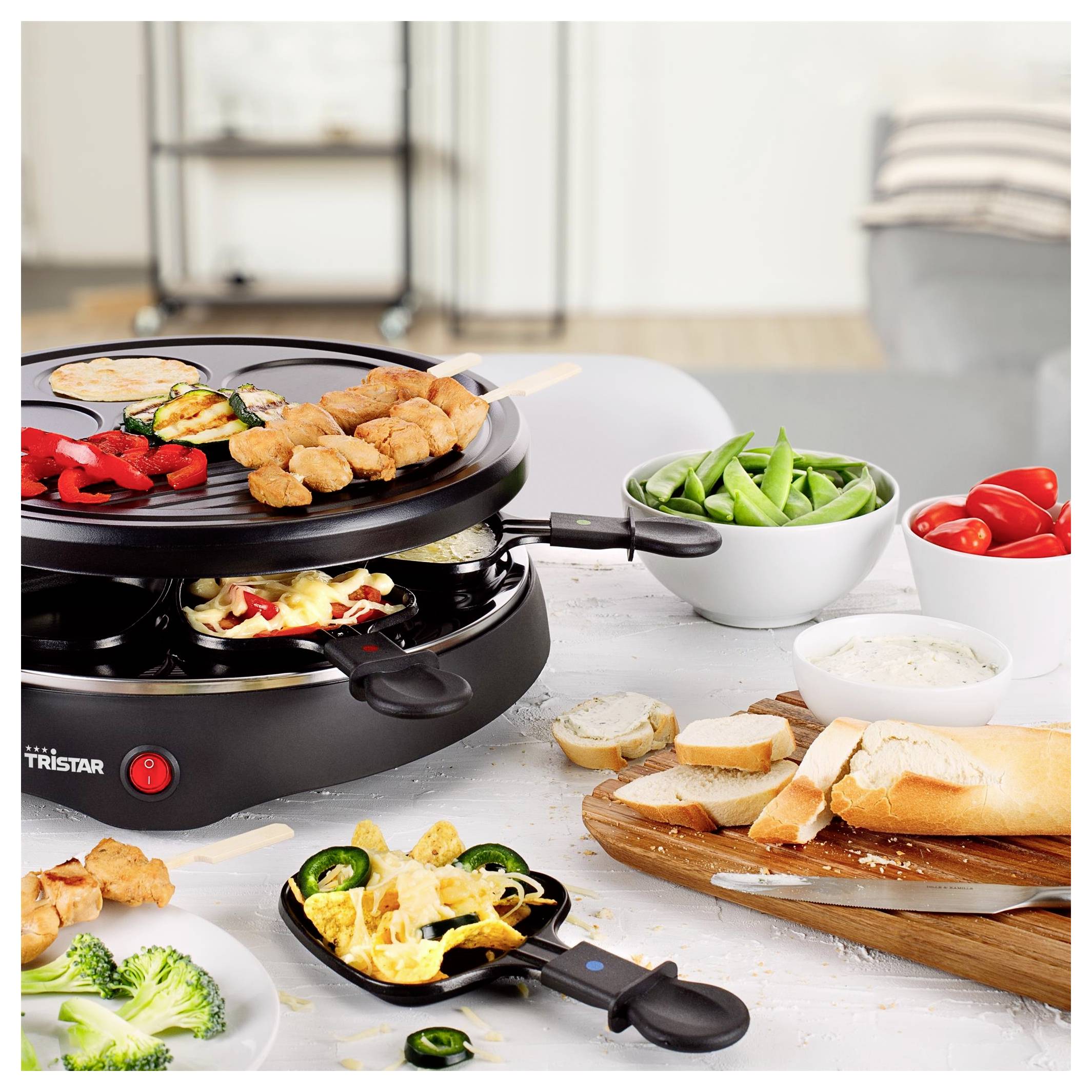 Gril de table d'intérieur avec de la viande et des légumes brochés, entouré de bols de pois gourmands et de tomates, de pain, de trempette et de plats d'accompagnement.