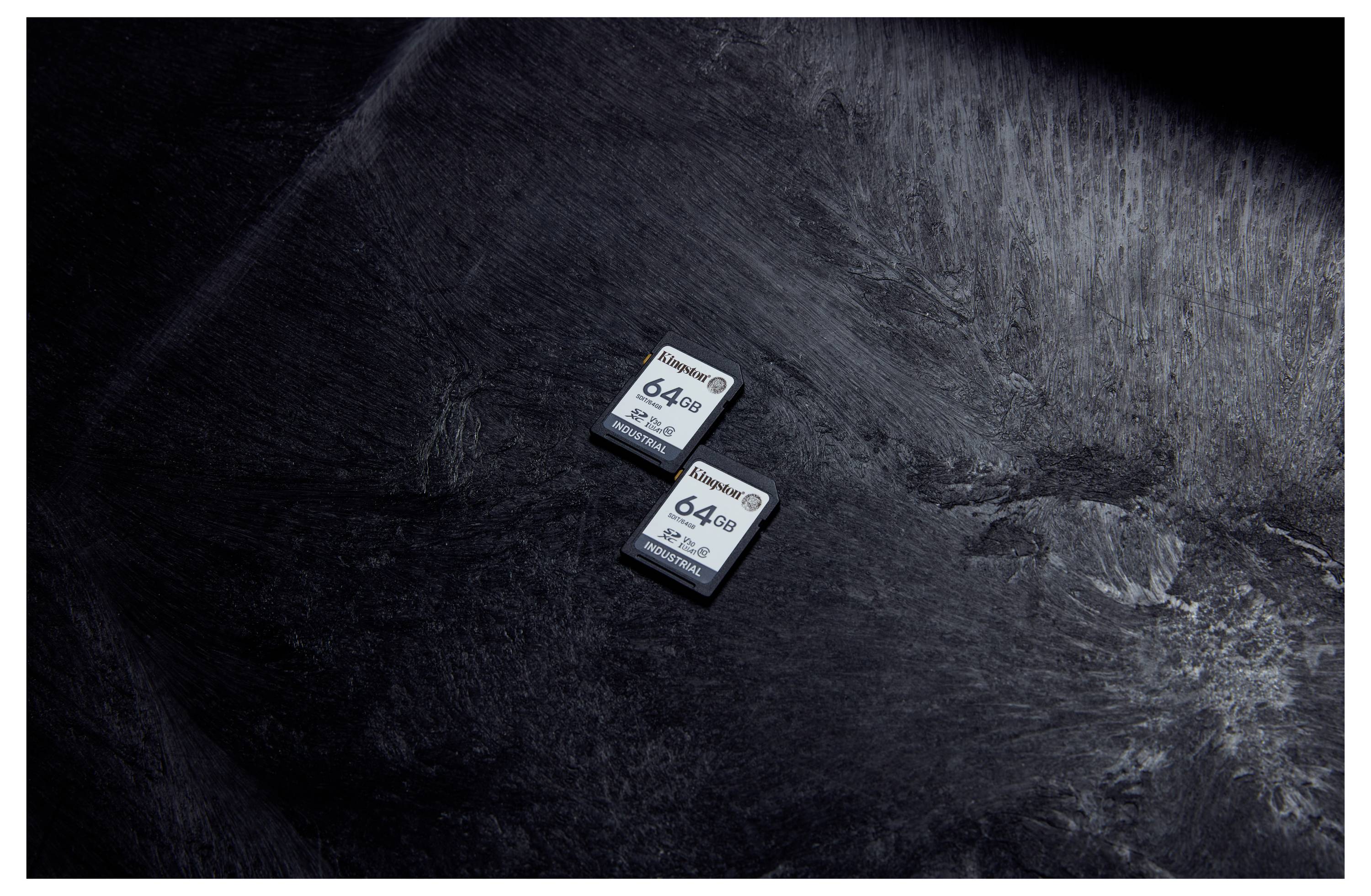 Deux cartes mémoire de 64 Go reposent sur une surface texturée sombre, vues de dessus.