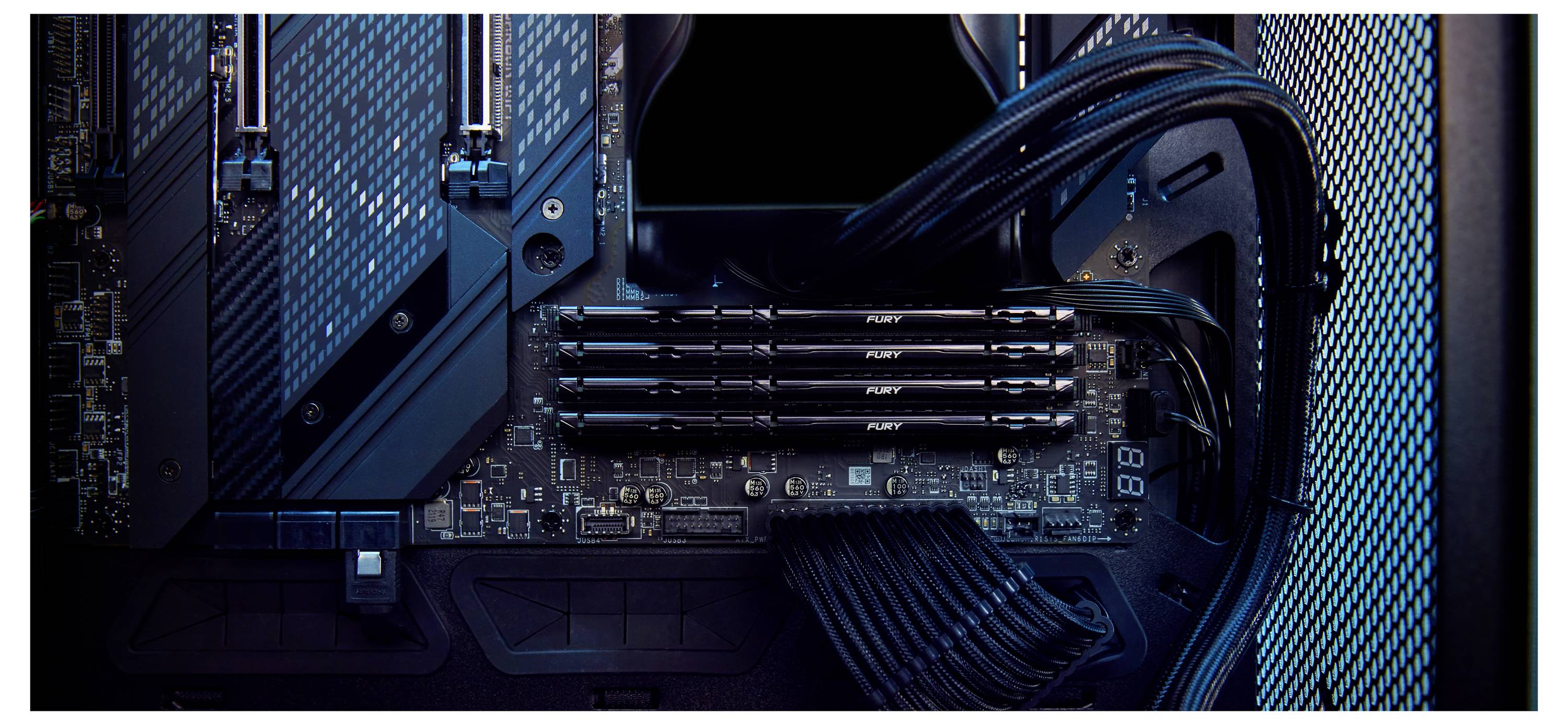Gros plan d'une carte mère de PC de gaming de bureau avec RAM, câbles et composants illuminés à l'intérieur du boîtier.