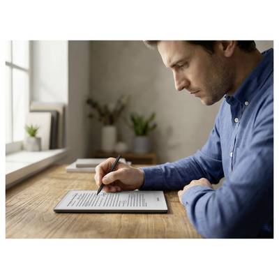 Un homme en chemise bleue signe un document sur un presse-papiers à un bureau en bois près d'une fenêtre, dans un cadre de bureau à domicile.