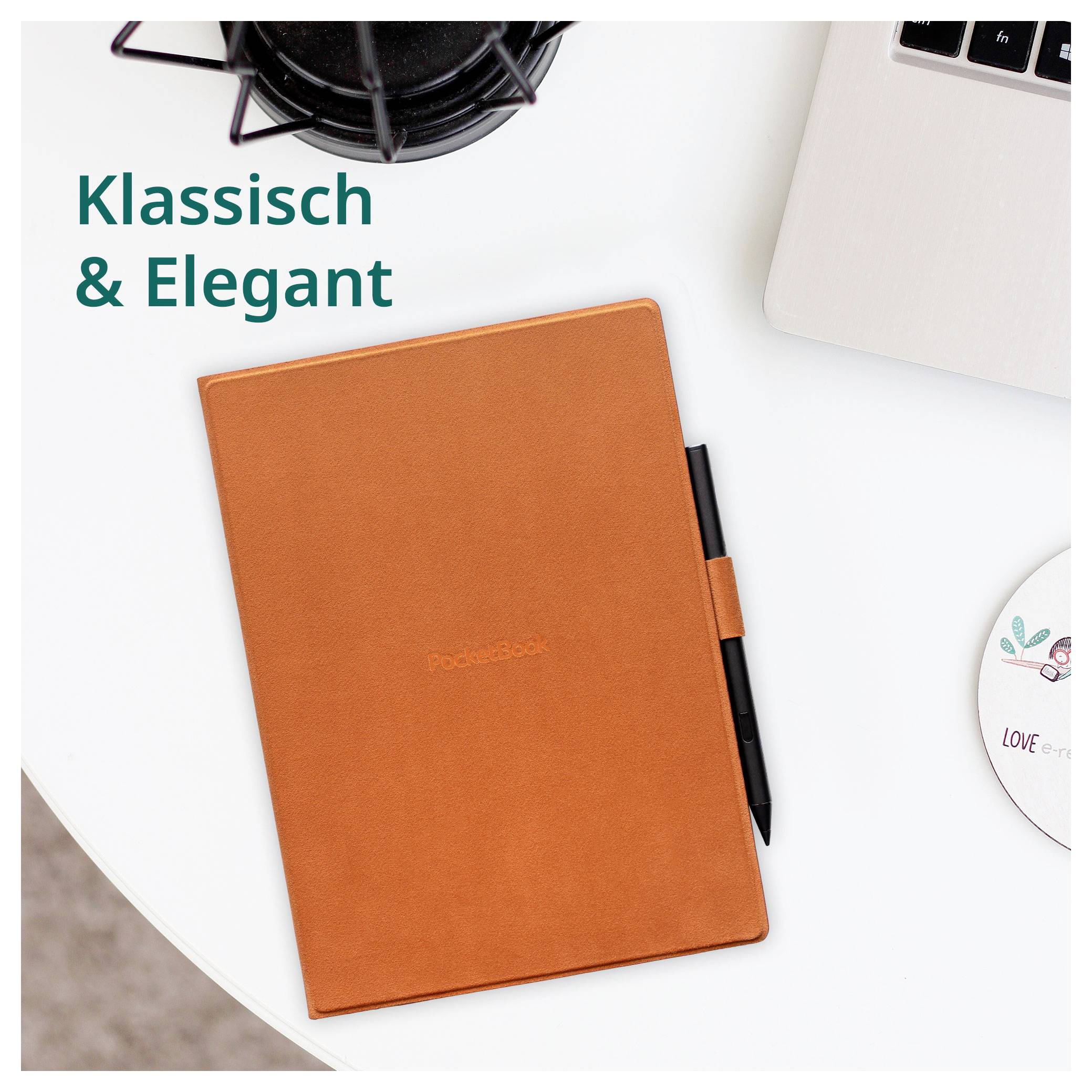 Carnet de cuir orange avec un stylo sur un bureau blanc, portant l'étiquette « Klassisch & Elegant », à côté d'un ordinateur portable et d'une tasse de café