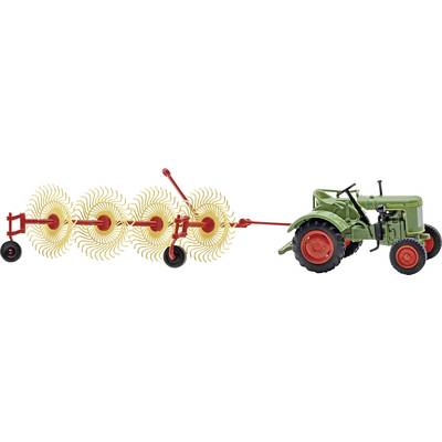 Un tracteur vert tire une fraise rotative rouge, avec des dents rotatives montrées en train de couper et d'ameublir le sol derrière elle.
