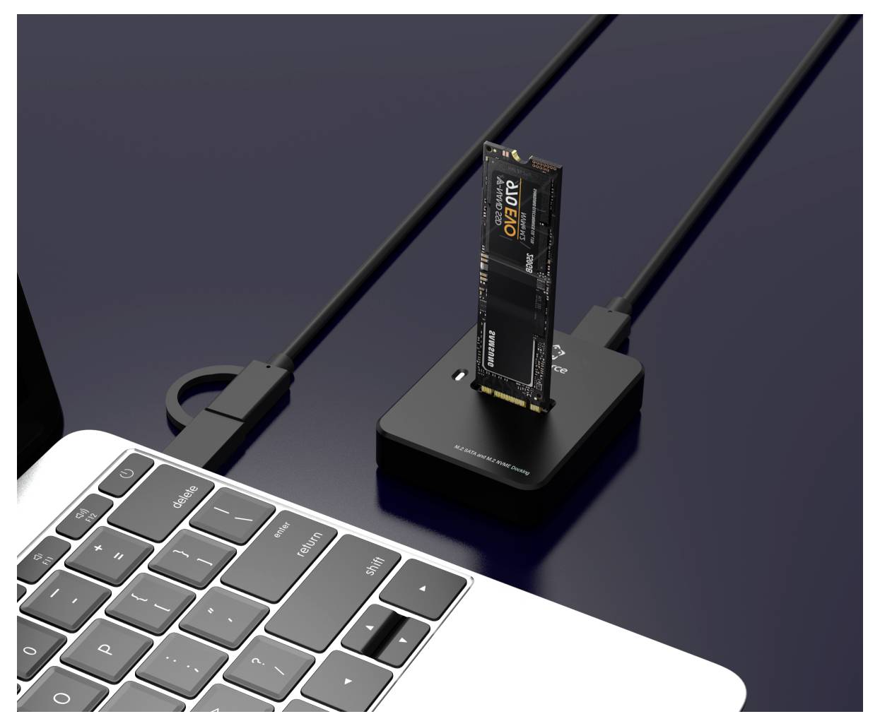 Petit SSD externe branché dans un dock compact noir situé à côté du clavier d'un ordinateur portable, avec des câbles connectés sur un bureau foncé.