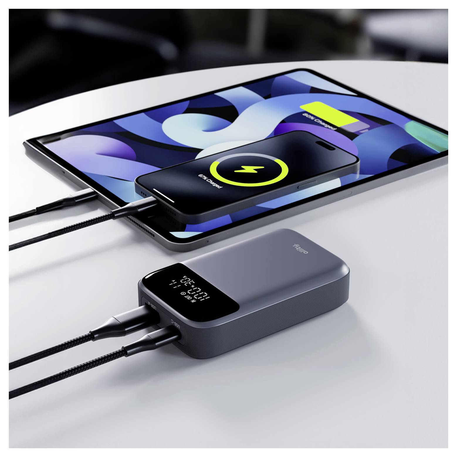 Configuration de charge sans fil avec un smartphone en charge sur une tablette, reliés par des câbles à une batterie externe portable sur un plan de travail.