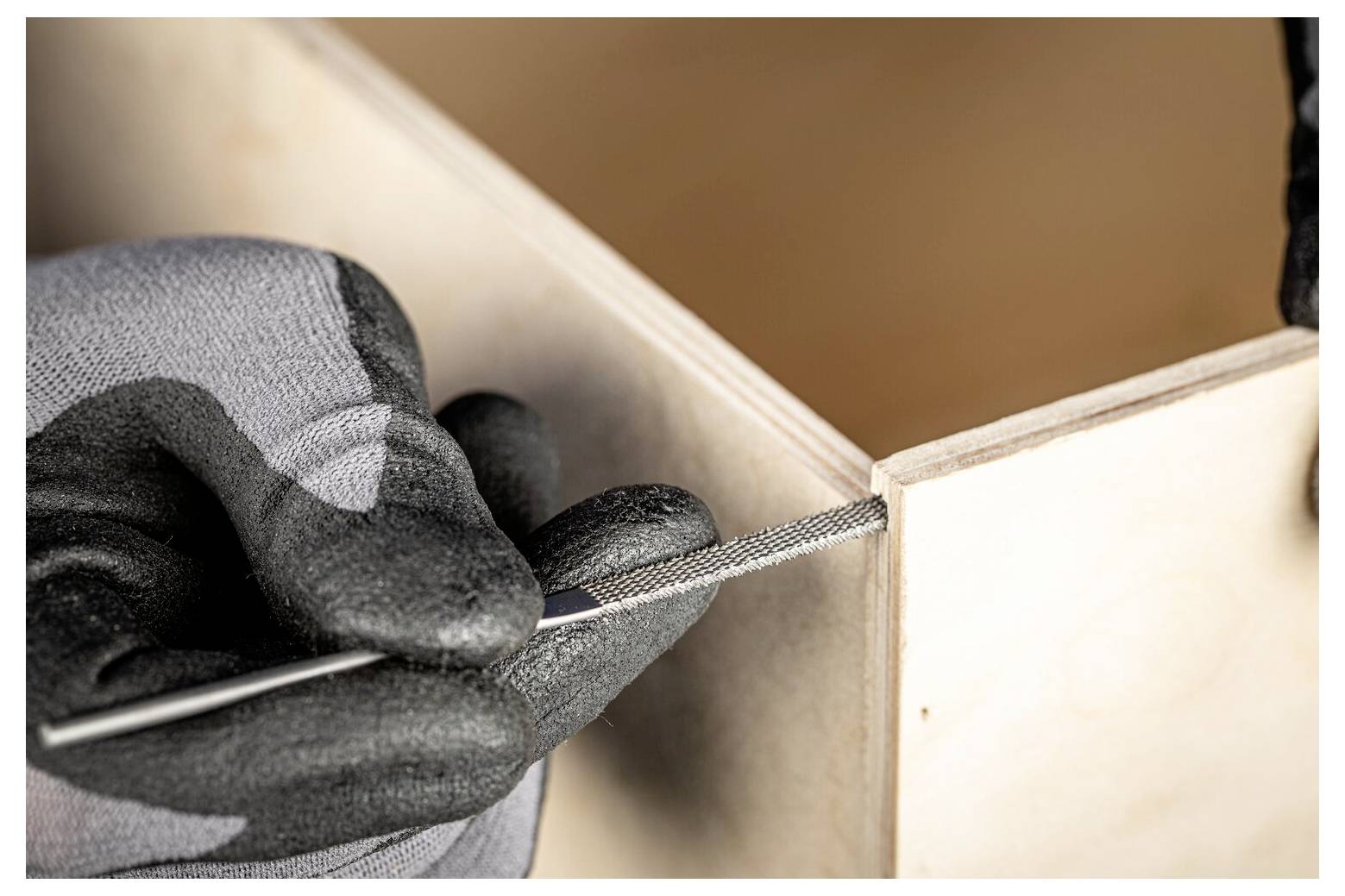 Main gantée utilisant une lime métallique pour lisser le coin intérieur d'un cadre de boîte en bois.