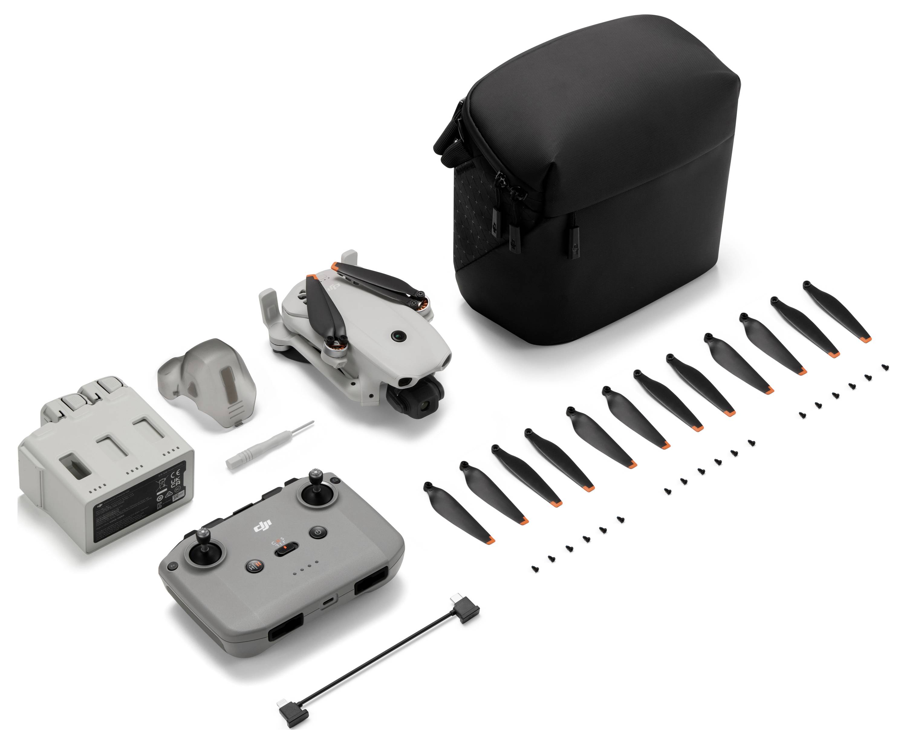 Kit de drone compact avec étui de transport, télécommande, batterie, chargeur, hélices de rechange et petits outils disposés sur un fond blanc.