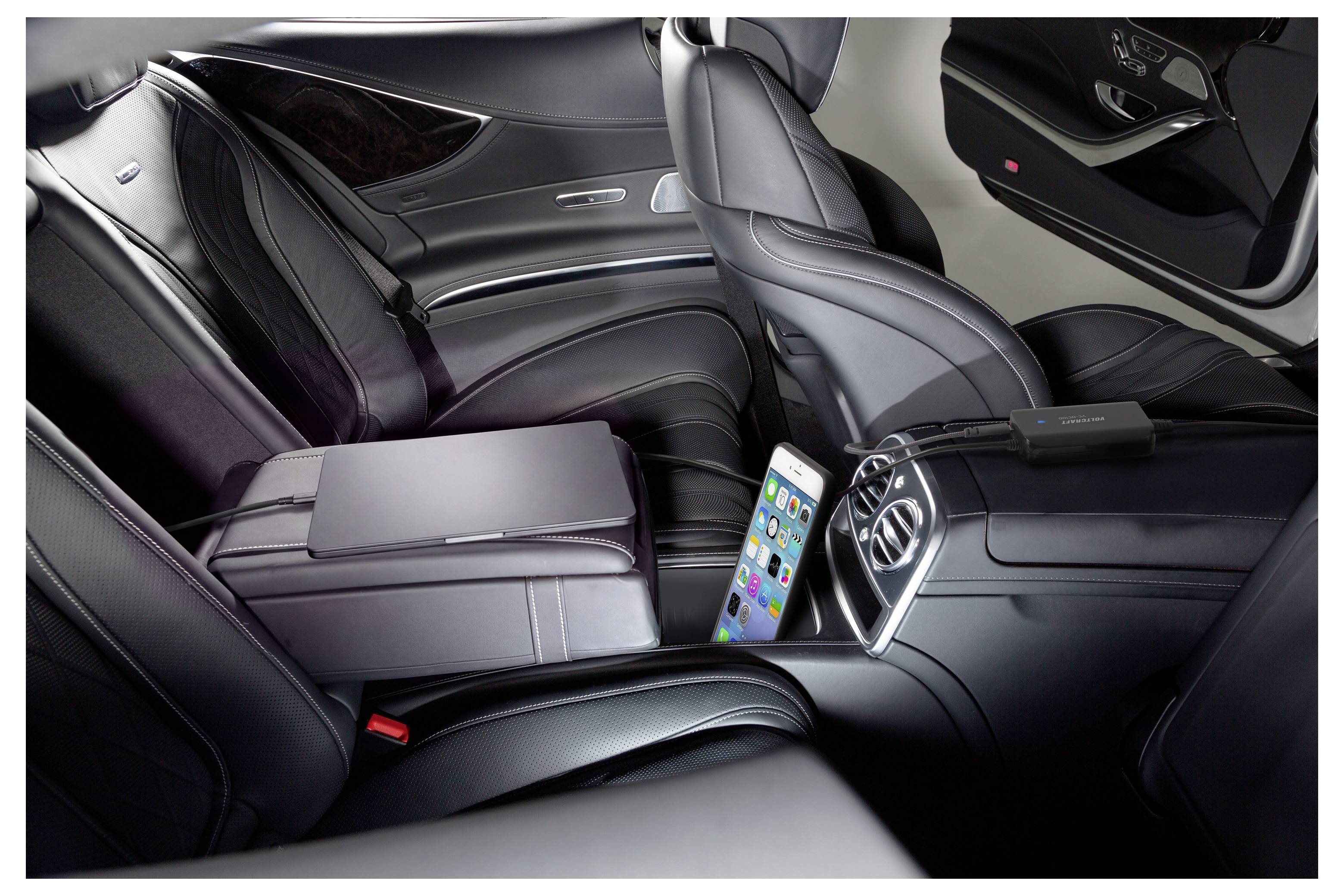 Siège arrière de voiture de luxe avec des sièges en cuir, une console centrale, et un smartphone posé verticalement à côté d'un ordinateur portable plié sur le siège.