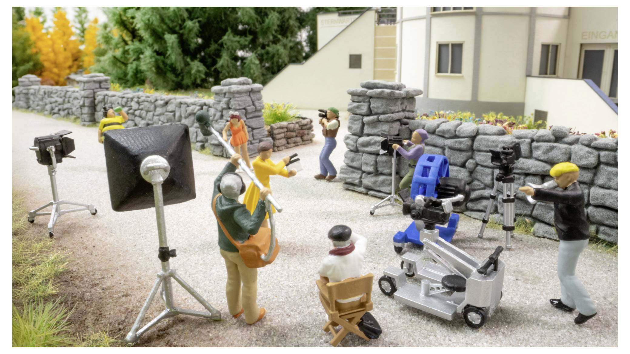 Ensemble de tournage miniature avec équipe et équipement de caméra filmant des acteurs près d'un mur en pierre à l'extérieur.