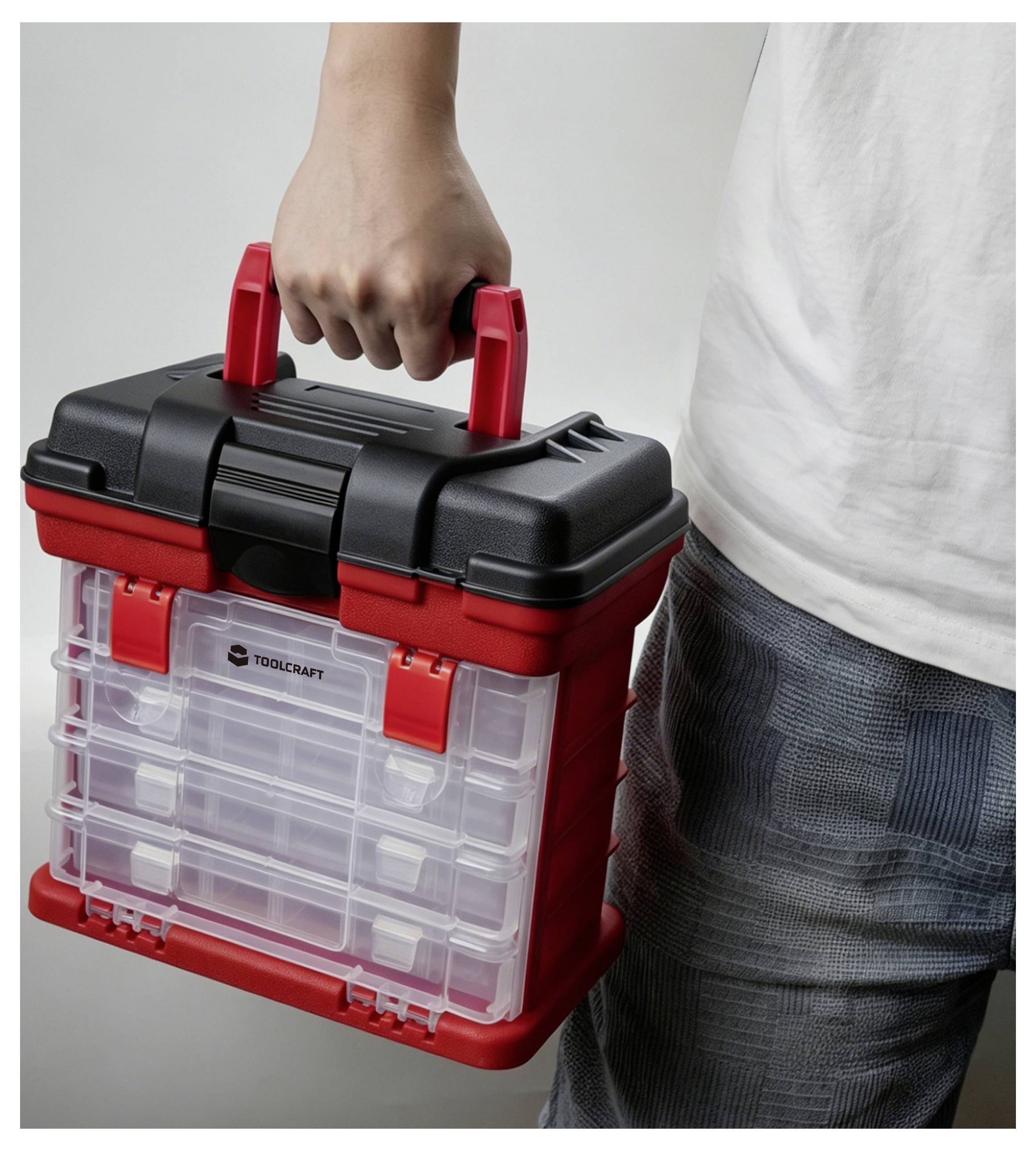 Personne tenant une boîte à outils de rangement en plastique rouge et noir Toolcraft par sa poignée.