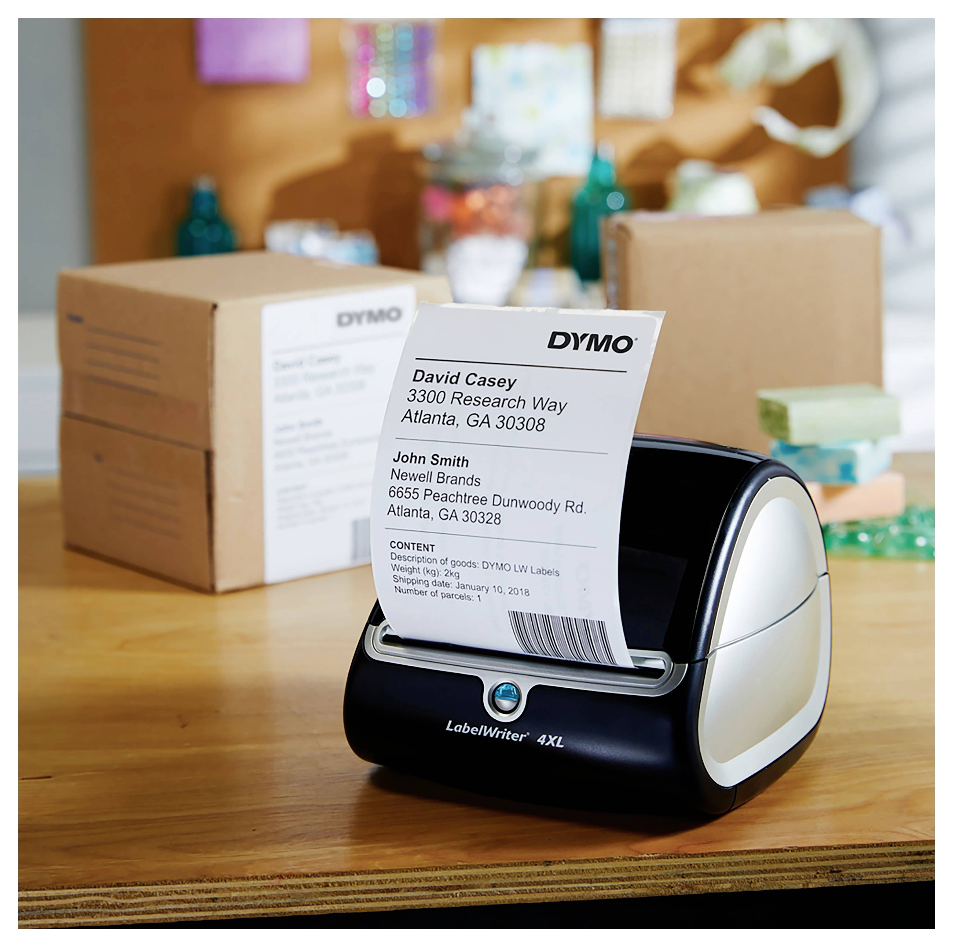 Imprimante DYMO LabelWriter 4XL imprimant une étiquette d'expédition avec des adresses de destinataire sur un bureau, avec des boîtes emballées en arrière-plan.