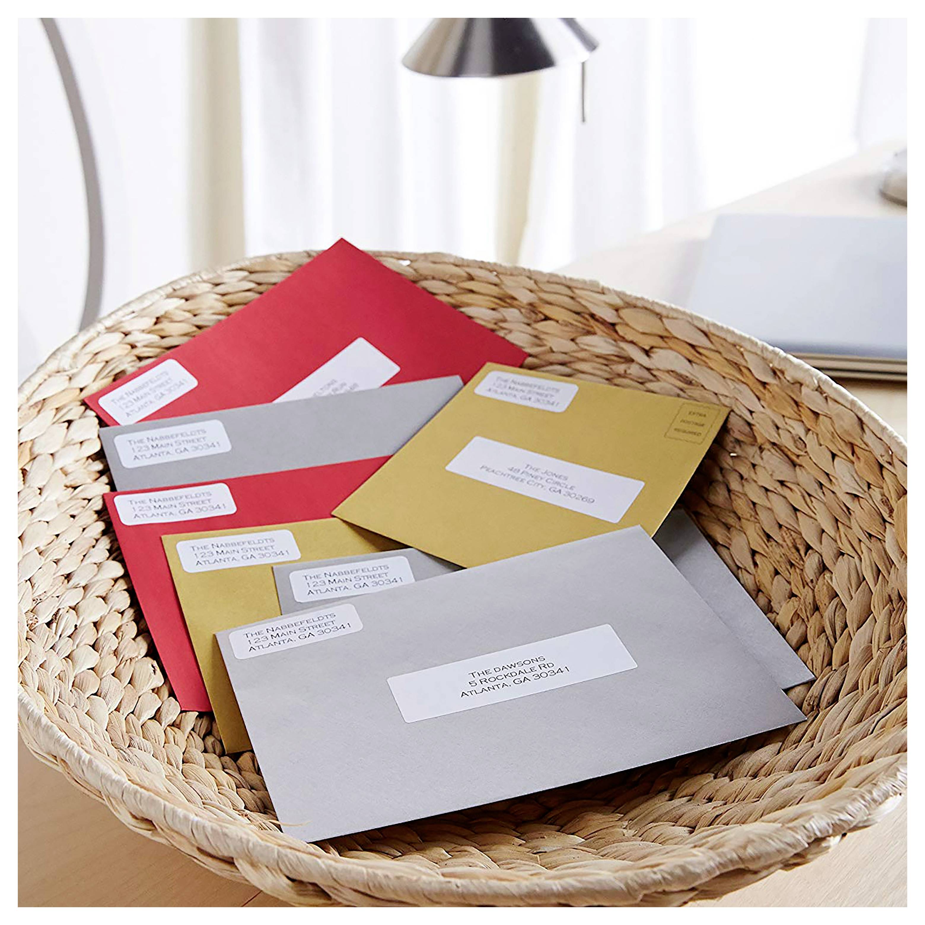 Panier tissé contenant plusieurs enveloppes adressées en rouge, gris, or et blanc sur un bureau.