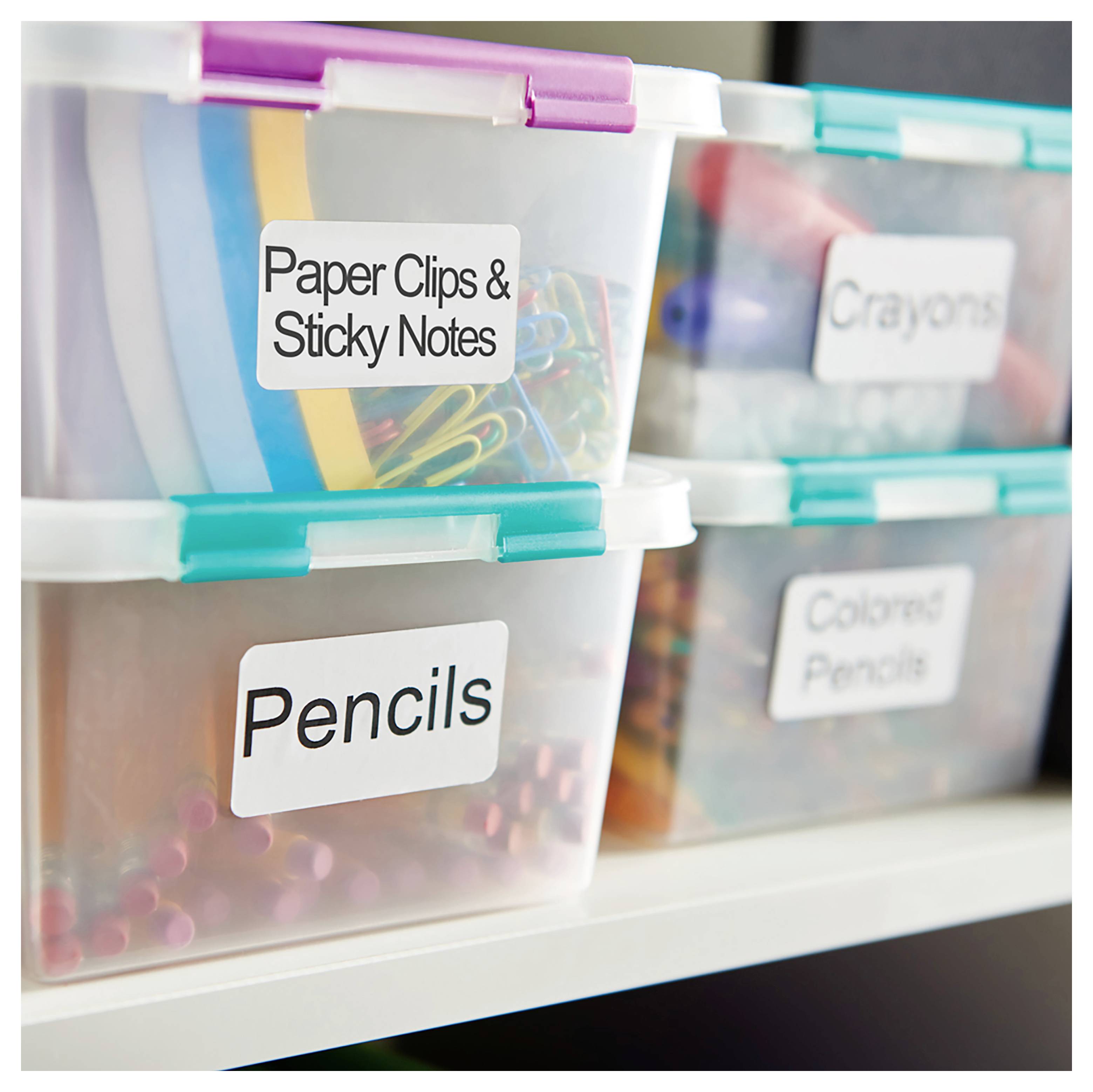 Des bacs de rangement empilables et transparents étiquetés « Trombones et Post-it », « Crayons », « Craies de couleur » et « Crayons de couleur » organisés sur une étagère.