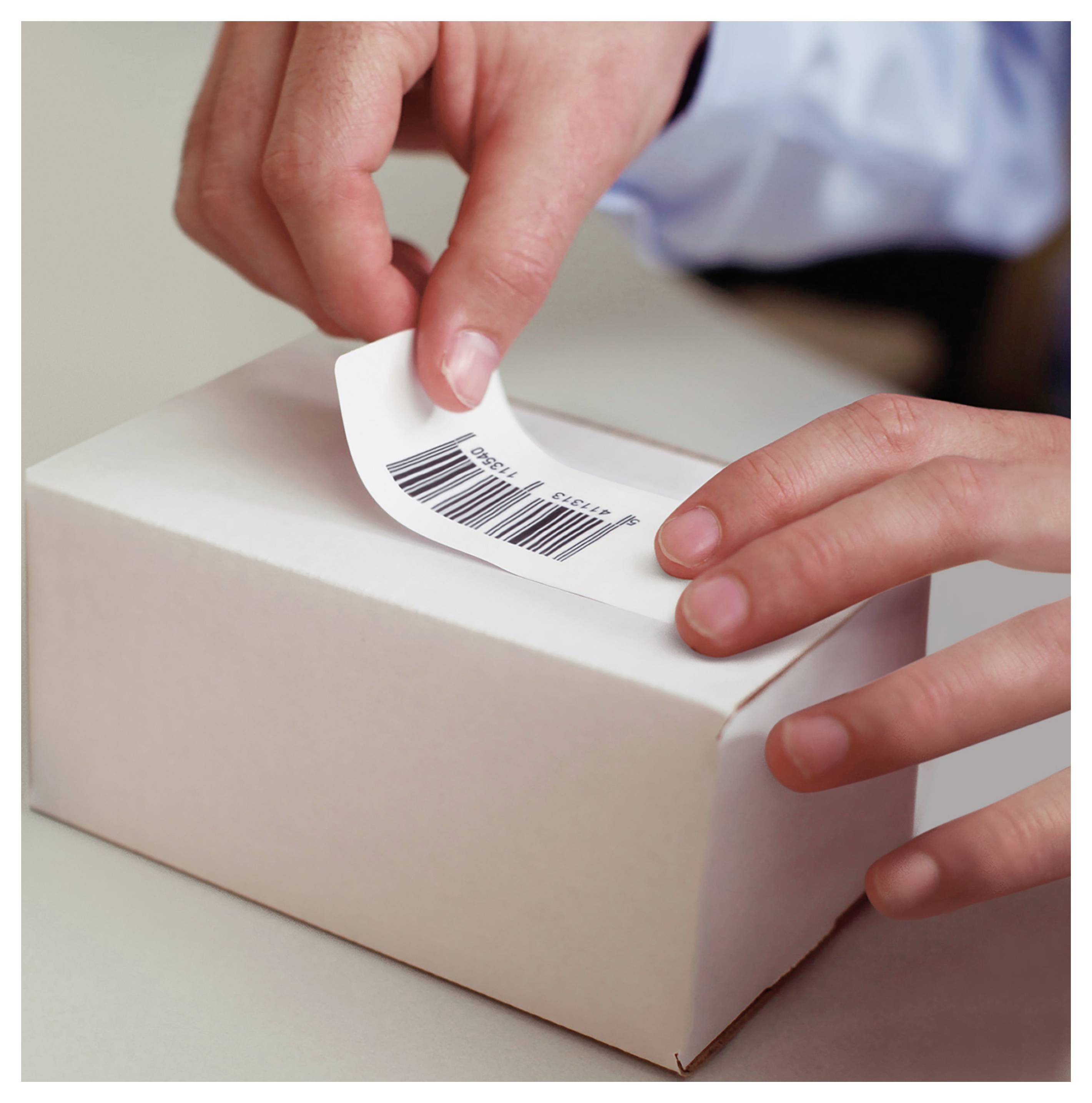 Mains appliquant une étiquette code-barres sur une petite boîte blanche, suggérant l'emballage de produits ou la préparation de l'expédition.
