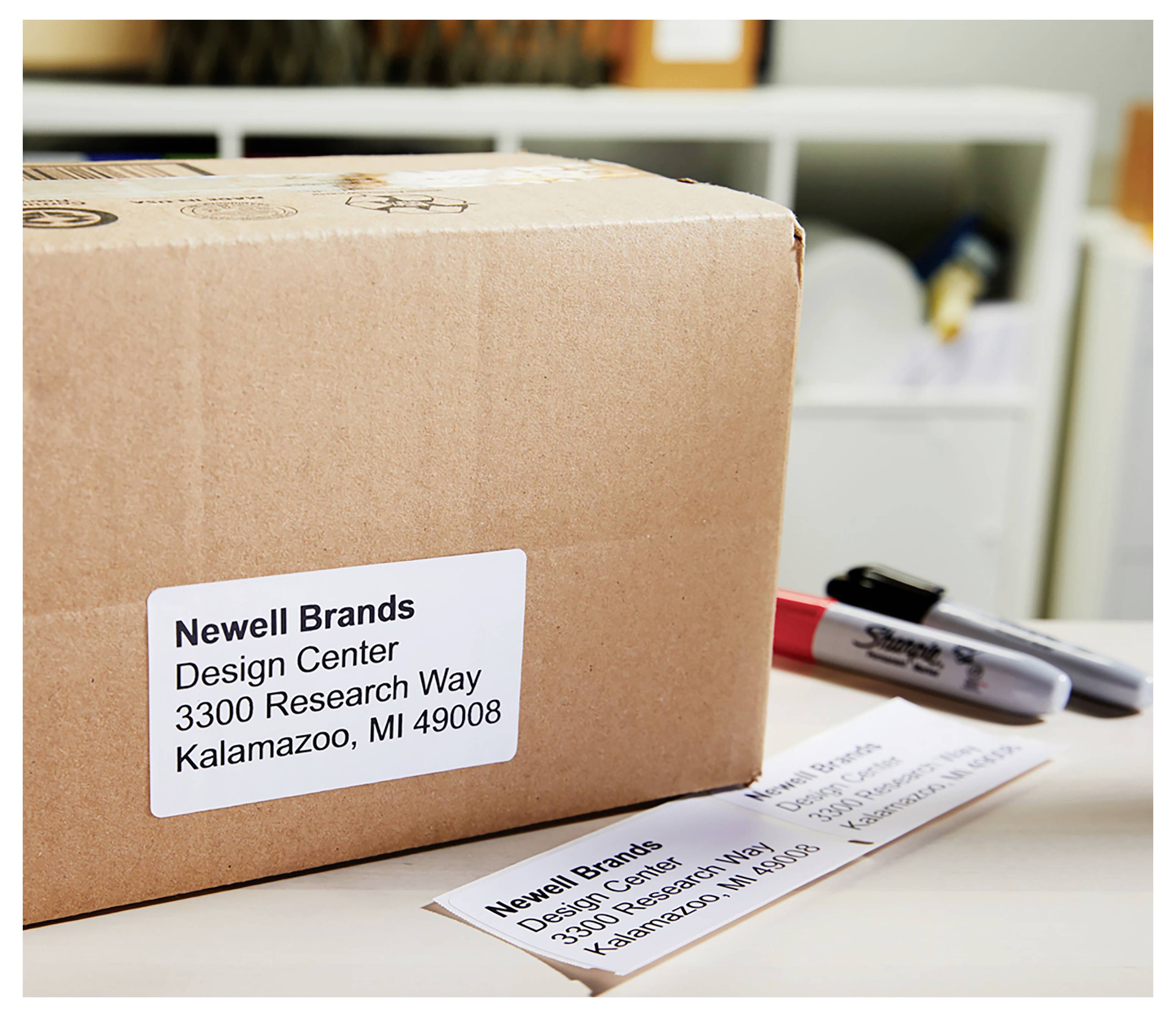 Une boîte d'expédition portant une étiquette adresse Newell Brands est posée sur un bureau à côté d'un marqueur et d'une deuxième étiquette d'expédition.
