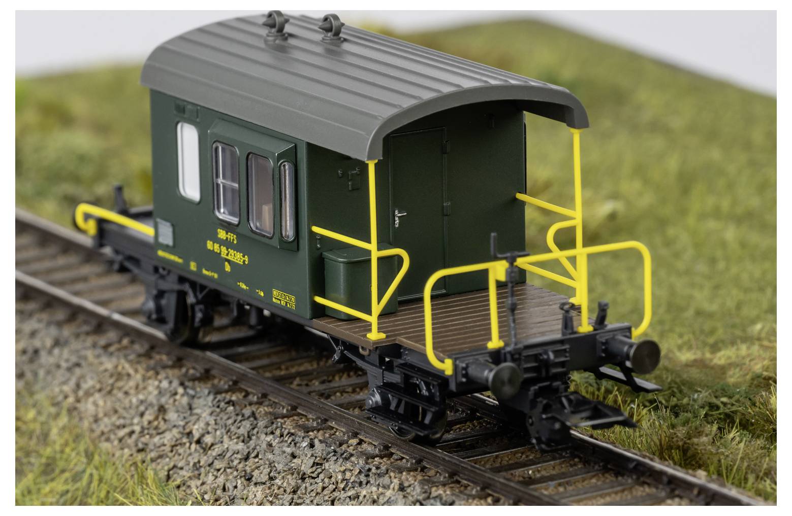 Wagon de queue de train miniature vert avec rampes jaunes sur les rails dans un paysage miniature herbeux.