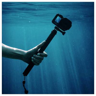 Main tenant un bâton de selfie avec une caméra d'action sous l'eau, avec des rayons de lumière bleus en arrière-plan.