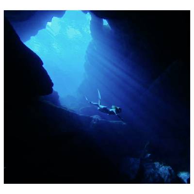 Un plongeur en apnée nageant à travers une grotte sous-marine sombre éclairée par une lumière bleue d'en haut.