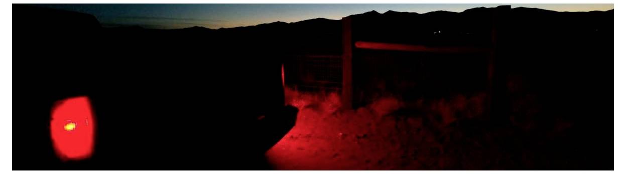 Paysage sombre au crépuscule avec une lumière rouge brillante et éclatante sur la gauche et une illumination rouge près d'une clôture ou d'un portail au centre.