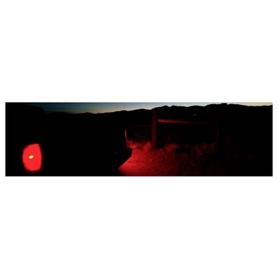 Paysage sombre au crépuscule avec une lumière rouge brillante et éclatante sur la gauche et une illumination rouge près d'une clôture ou d'un portail au centre.