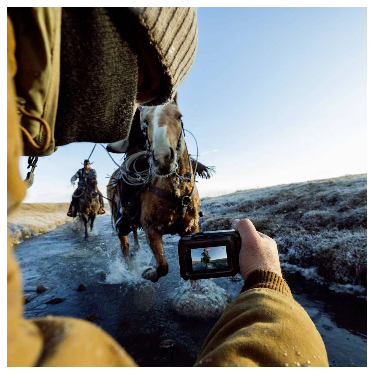 Personne vêtue de vêtements d'hiver filmant deux chevaux et cavaliers s'approchant sur une route de terre givrée avec une caméra portative.