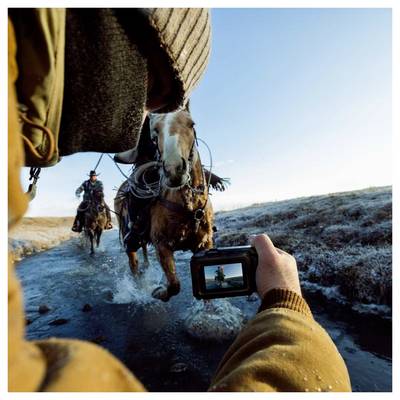 Personne vêtue de vêtements d'hiver filmant deux chevaux et cavaliers s'approchant sur une route de terre givrée avec une caméra portative.