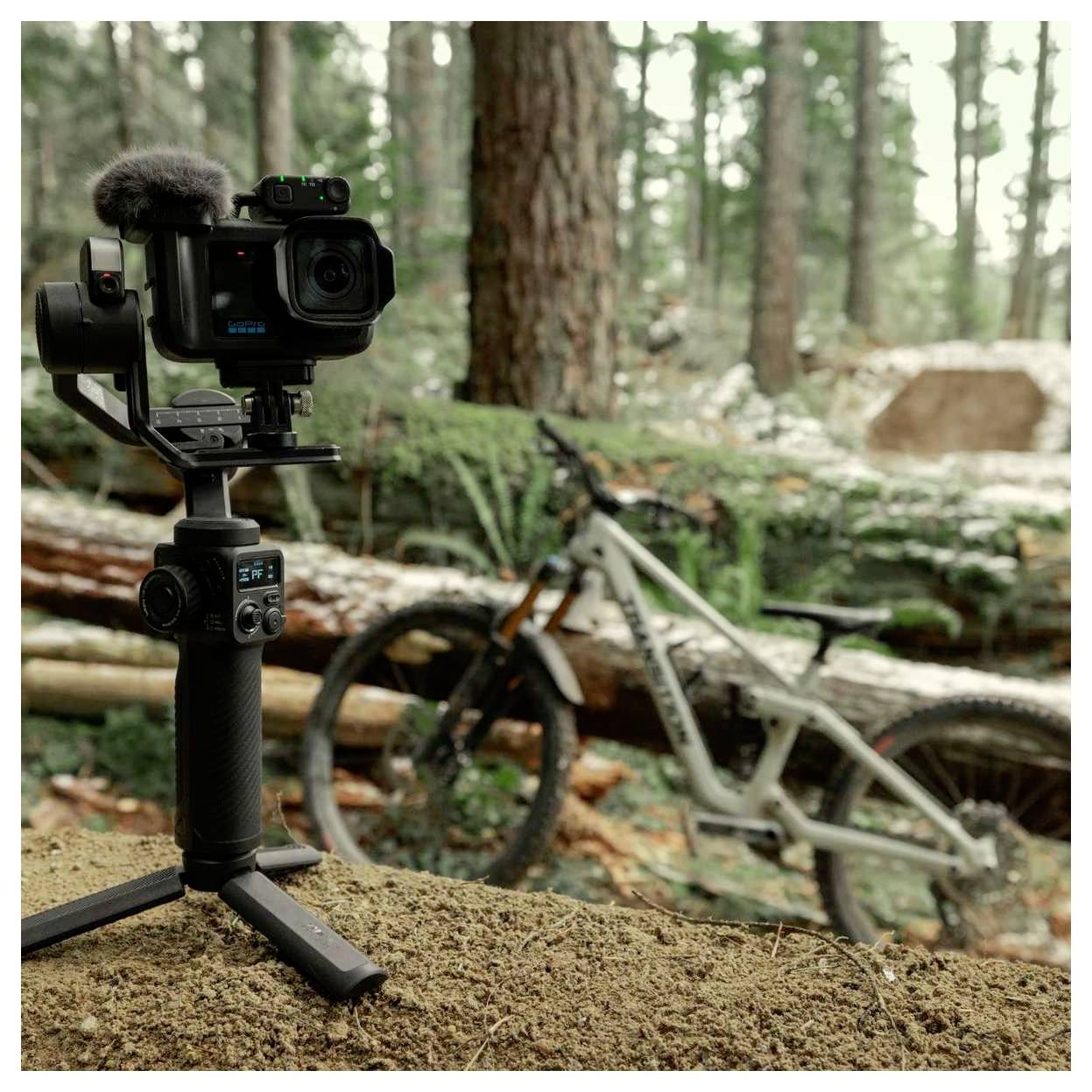 Caméra d'action montée sur un cardan/trépied dans une forêt, avec un vélo de montagne flou en arrière-plan sur une bûche.