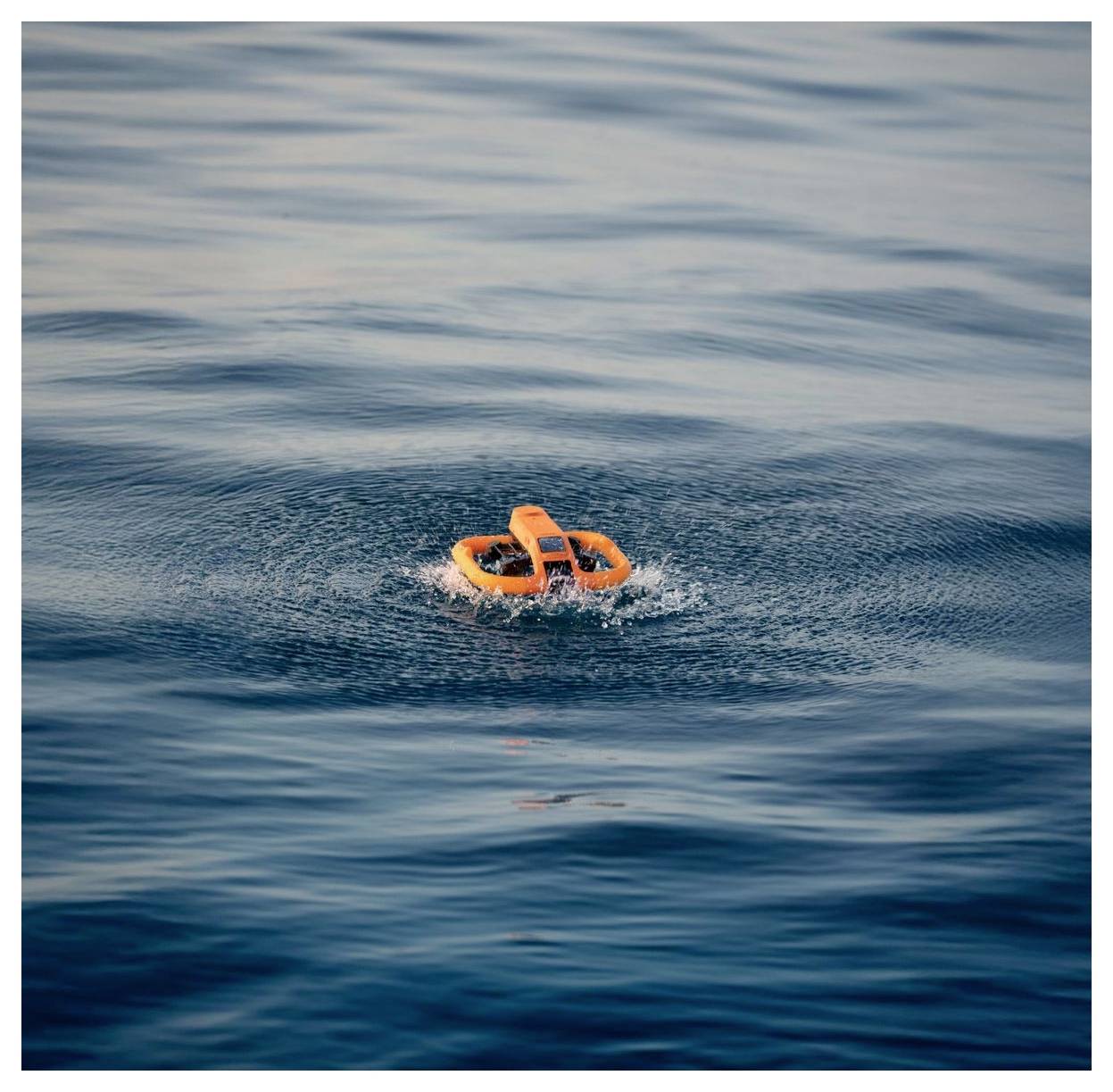 Anneau de sauvetage orange flottant seul sur une eau bleue calme, créant de petites ondulations.